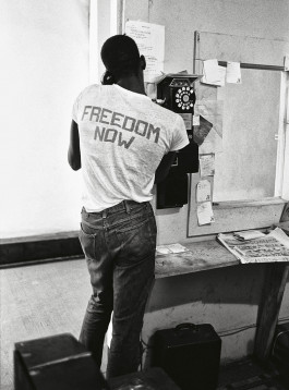 Camera Work exhibition, black and white photo of a black man with his back turned and talking on a pay phone in a room, the inscription on his T-shirt