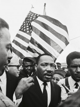 Camera Work exhibit, black and white photo of Martin Luther King Jr. making his way through a crowd of journalists, an American flag fluttering behind him