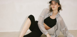 woman reclining on her side in black leggings, top, translucent blouse and cap 