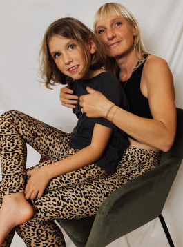 a woman sits on a chair in her arms with a little girl, the woman is wearing a black T-shirt and leopard leggings, and the girl is wearing a black T-shirt and leopard leggings